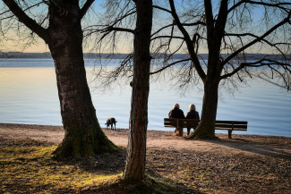 2 ältere Menschen mit Hund sitzen auf einer Bank am See